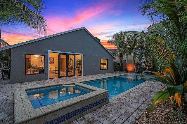 pool at dusk with a patio and an in ground hot tub