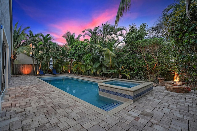 pool at dusk featuring a patio area, an in ground hot tub, and a fire pit