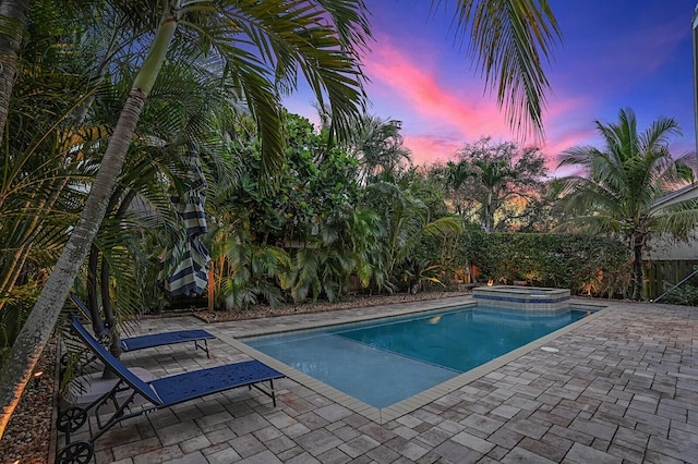 pool at dusk featuring a patio area and an in ground hot tub