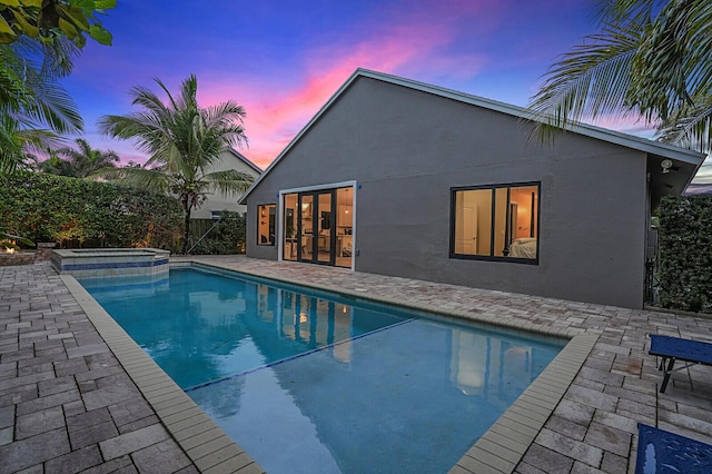 pool at dusk with a patio and an in ground hot tub