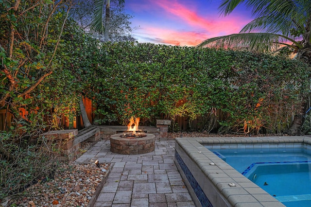 pool at dusk with an outdoor fire pit and an in ground hot tub