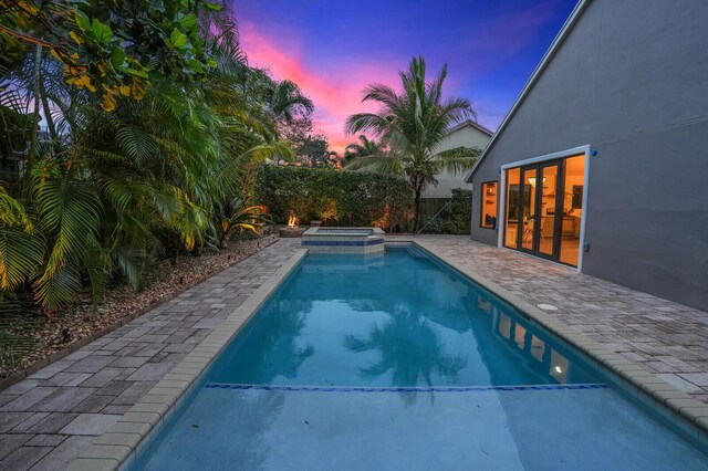 pool at dusk with a patio and an in ground hot tub