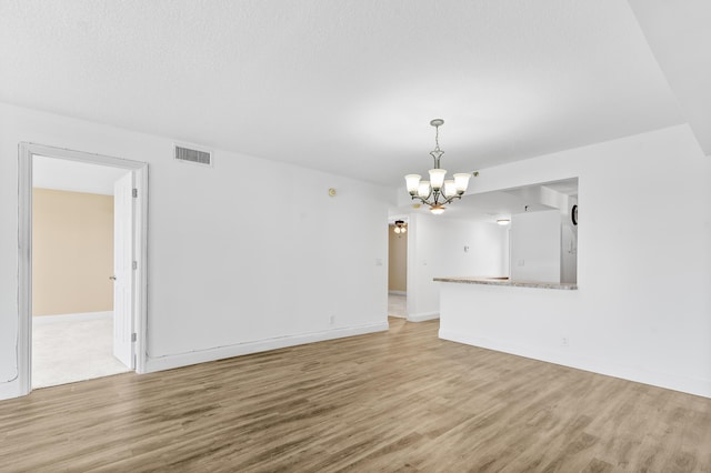 unfurnished living room with an inviting chandelier and light hardwood / wood-style flooring