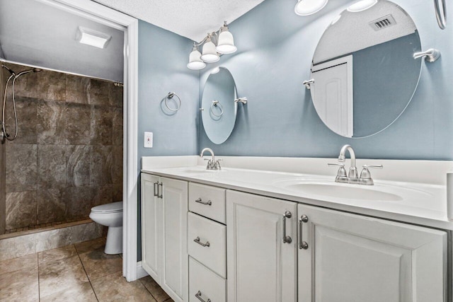 bathroom with a textured ceiling, toilet, vanity, and a tile shower