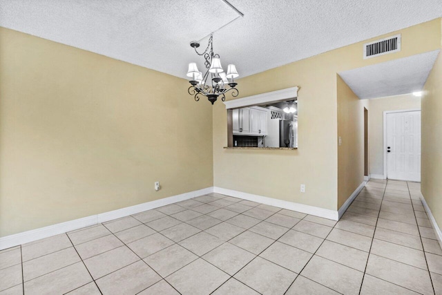 empty room featuring light tile patterned flooring, a chandelier, and a textured ceiling