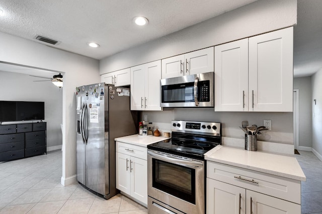 kitchen with light tile patterned floors, white cabinetry, ceiling fan, appliances with stainless steel finishes, and light stone counters