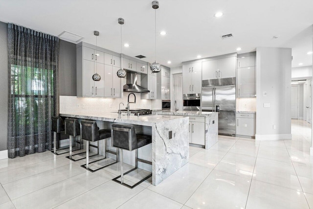 kitchen featuring decorative light fixtures, a breakfast bar area, decorative backsplash, stainless steel appliances, and wall chimney range hood