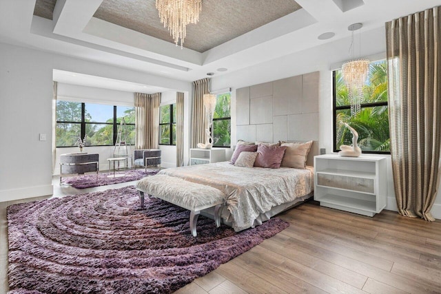 bedroom with multiple windows, light hardwood / wood-style floors, a raised ceiling, and a chandelier