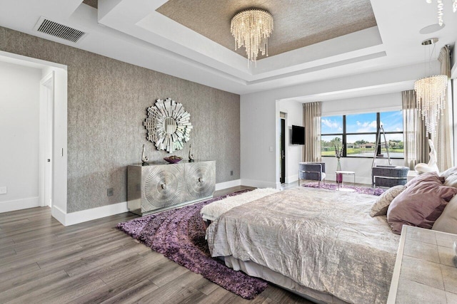 bedroom with an inviting chandelier, a tray ceiling, and hardwood / wood-style flooring