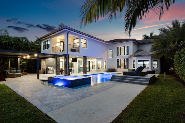 back house at dusk with a swimming pool with hot tub, an outdoor living space, a patio area, and a balcony