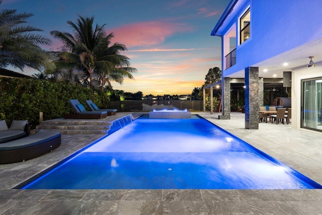 pool at dusk featuring a patio and pool water feature