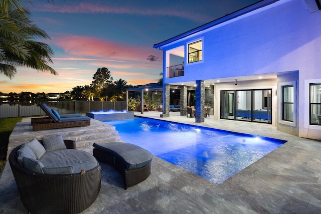 pool at dusk with pool water feature, a jacuzzi, and a patio