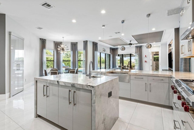 kitchen featuring pendant lighting, white cabinetry, sink, a large island with sink, and light stone countertops