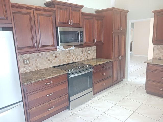 kitchen with backsplash, stainless steel appliances, light tile patterned flooring, and dark stone counters