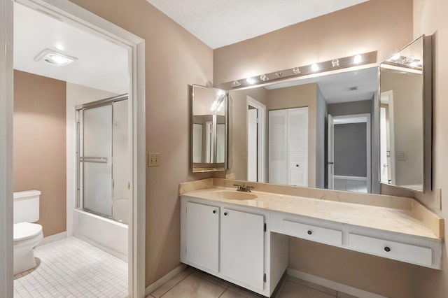 bathroom with bath / shower combo with glass door, toilet, vanity, baseboards, and tile patterned floors