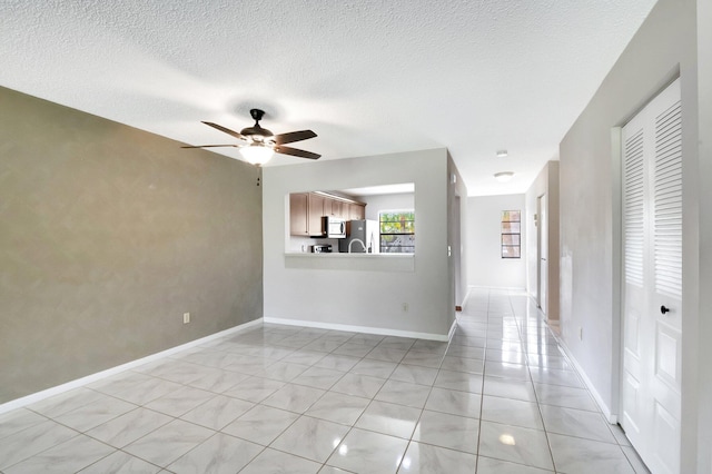 unfurnished room featuring light tile patterned floors, a textured ceiling, baseboards, and a ceiling fan