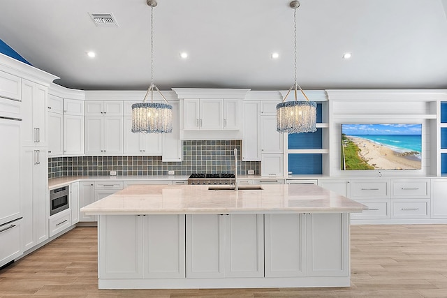 kitchen with decorative backsplash, an island with sink, white cabinets, and light stone countertops