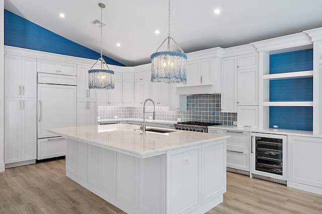 kitchen with tasteful backsplash, wine cooler, an island with sink, sink, and vaulted ceiling