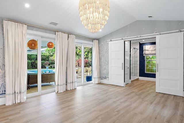 spare room with light hardwood / wood-style flooring, lofted ceiling, a barn door, and a notable chandelier