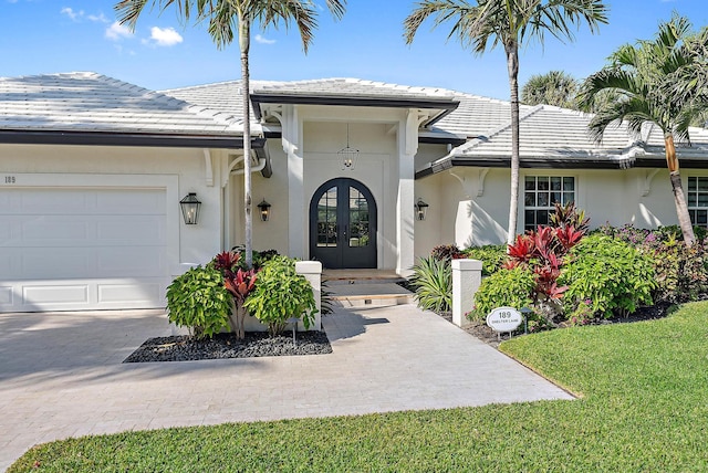 entrance to property featuring a garage, a lawn, and french doors