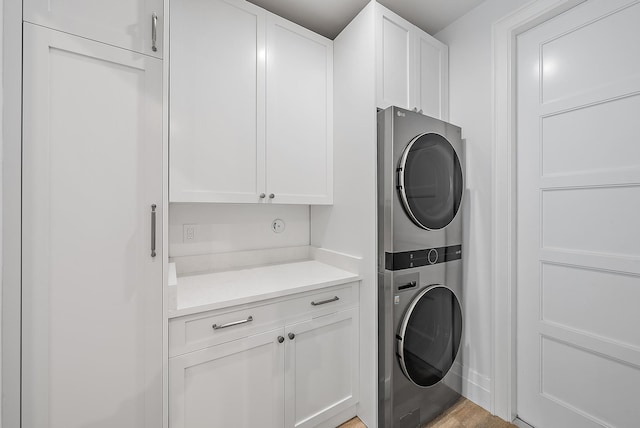 washroom with stacked washing maching and dryer, cabinets, and light hardwood / wood-style floors