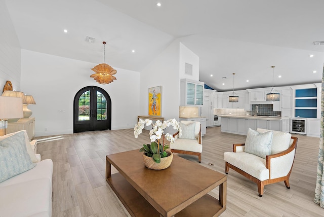 living room with wine cooler, sink, light hardwood / wood-style flooring, high vaulted ceiling, and french doors