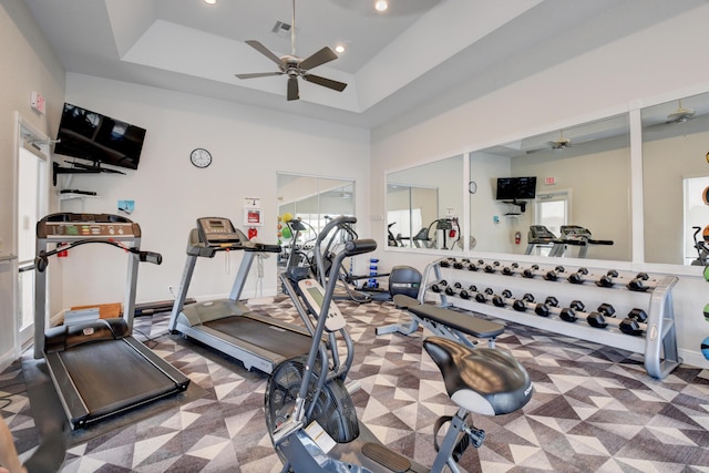 gym featuring a raised ceiling, ceiling fan, and a high ceiling