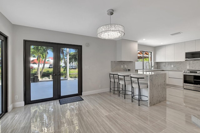 kitchen with decorative backsplash, stainless steel appliances, hanging light fixtures, and white cabinets