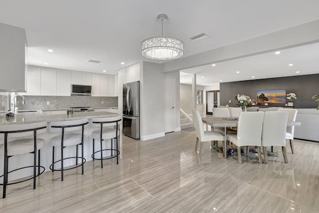 interior space with decorative light fixtures, white cabinetry, sink, a kitchen bar, and stainless steel appliances