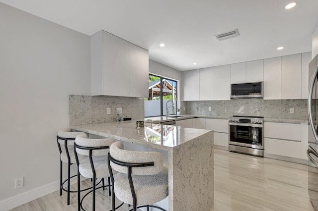 kitchen featuring a breakfast bar, white cabinetry, stainless steel appliances, light stone countertops, and kitchen peninsula