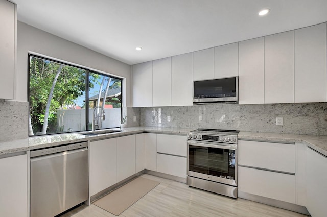 kitchen featuring appliances with stainless steel finishes, sink, white cabinets, decorative backsplash, and light stone counters