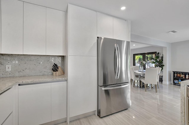 kitchen with stainless steel refrigerator, backsplash, light stone countertops, and white cabinets