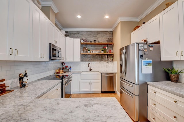 kitchen with sink, white cabinetry, ornamental molding, appliances with stainless steel finishes, and light stone countertops