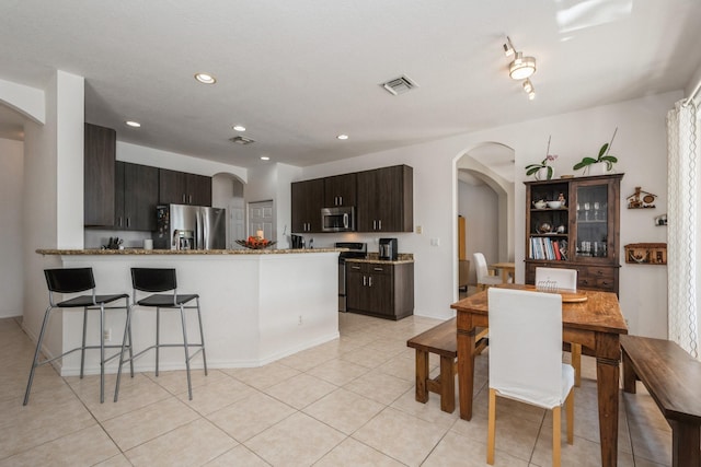 kitchen with light tile patterned floors, dark brown cabinetry, appliances with stainless steel finishes, and kitchen peninsula