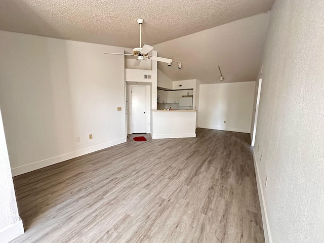 unfurnished living room with a textured ceiling, ceiling fan, vaulted ceiling, and hardwood / wood-style flooring