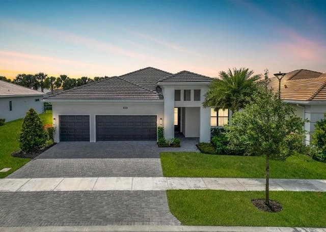 view of front of house with decorative driveway, a yard, an attached garage, and stucco siding