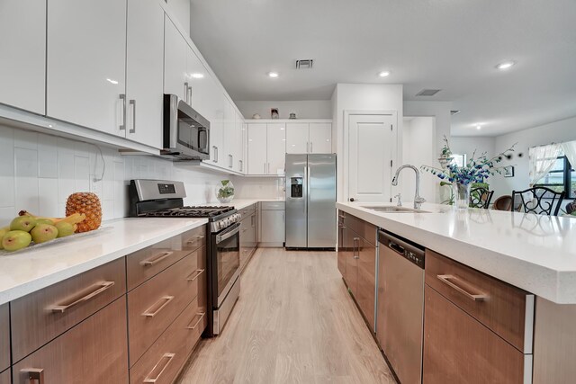 kitchen with stainless steel appliances, light hardwood / wood-style floors, a kitchen island with sink, and white cabinets