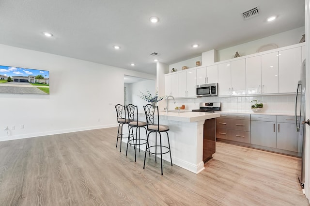 kitchen with a breakfast bar area, stainless steel appliances, visible vents, light wood-style flooring, and a sink