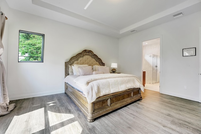 bedroom featuring hardwood / wood-style floors, connected bathroom, and a tray ceiling