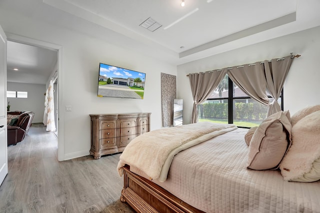 bedroom featuring light wood finished floors, a raised ceiling, visible vents, and baseboards