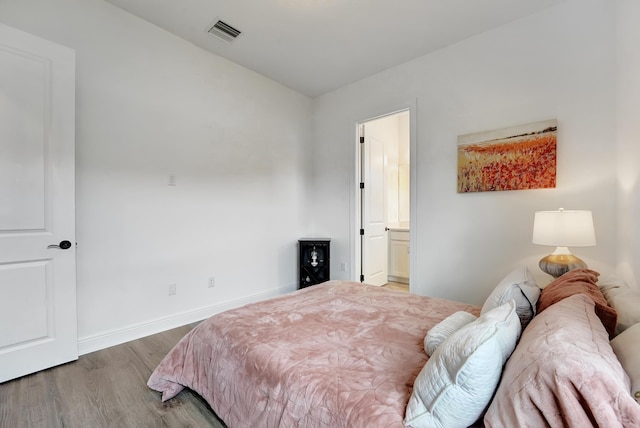 bedroom with ensuite bath and hardwood / wood-style floors