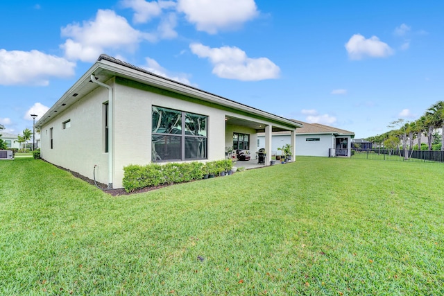 rear view of house with a patio, a lawn, fence, and stucco siding