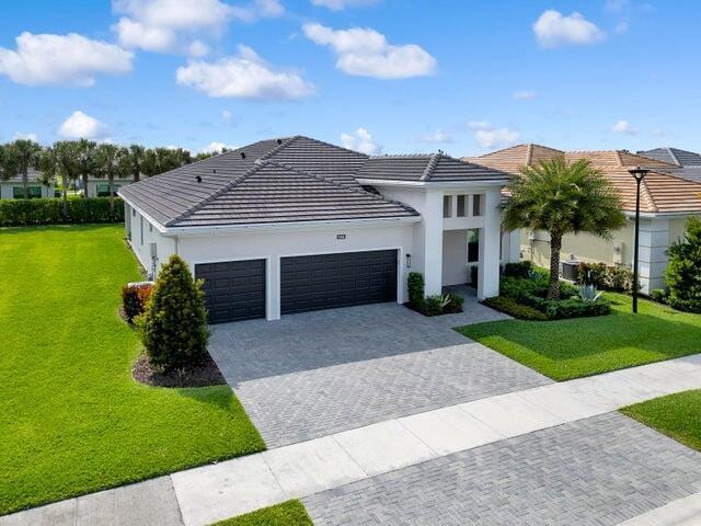 view of front of home with an attached garage, a tiled roof, decorative driveway, stucco siding, and a front lawn