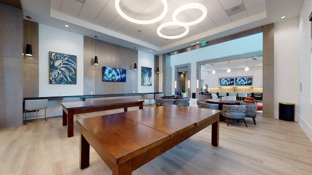 rec room featuring a tray ceiling, a high ceiling, and light wood-style floors