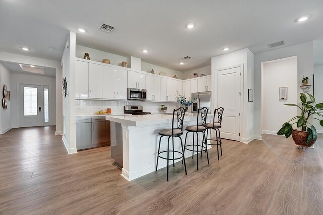 kitchen featuring light hardwood / wood-style flooring, a breakfast bar area, stainless steel appliances, white cabinets, and a center island with sink