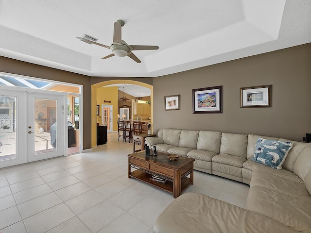 living room featuring ceiling fan, light tile patterned floors, a tray ceiling, and french doors