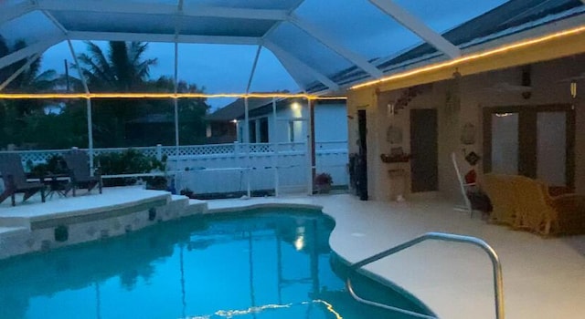 pool at dusk featuring glass enclosure and a patio