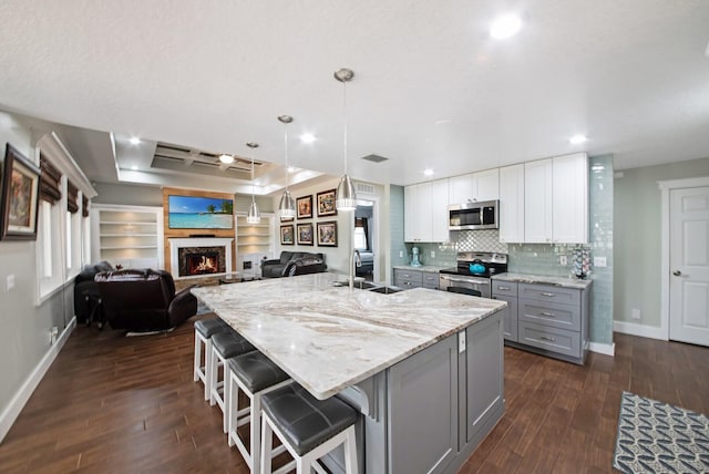 kitchen with pendant lighting, appliances with stainless steel finishes, gray cabinetry, a kitchen breakfast bar, and white cabinets