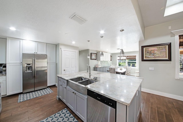 kitchen featuring sink, appliances with stainless steel finishes, light stone countertops, a center island with sink, and decorative light fixtures