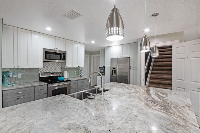 kitchen featuring sink, light stone counters, hanging light fixtures, stainless steel appliances, and white cabinets